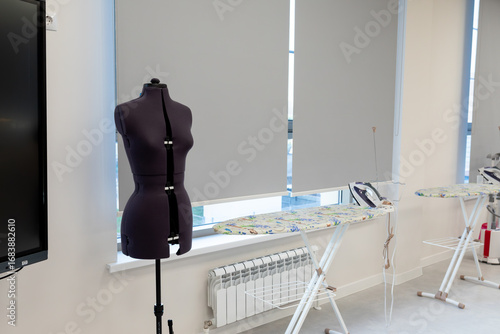 Tailor's dummy and sewing equipment in a bright workspace. Tailor's dummy, ironing boards in a modern sewing workshop. Photo