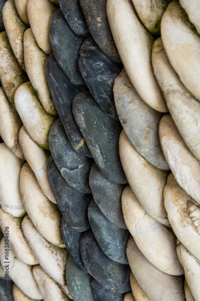 Obraz premium Detailed side view of a natural stone mosaic made of smooth, rounded black and cream pebbles. Abstract texture and pattern, ideal for backgrounds