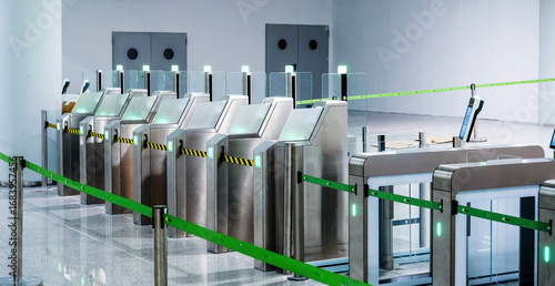 Modern automated passport control gates with glass barriers, scanners, and glowing green lights in empty airport checkpoint hall