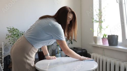 A woman cleans and dusts her house with a rag
