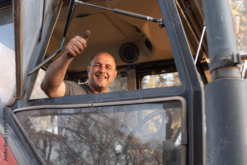 Trabajador operario en maquinaria agrícola mirando a cámara sonriente con gesto de aprobación, primer plano dedo pulgar en alto y sonrisa amplia
