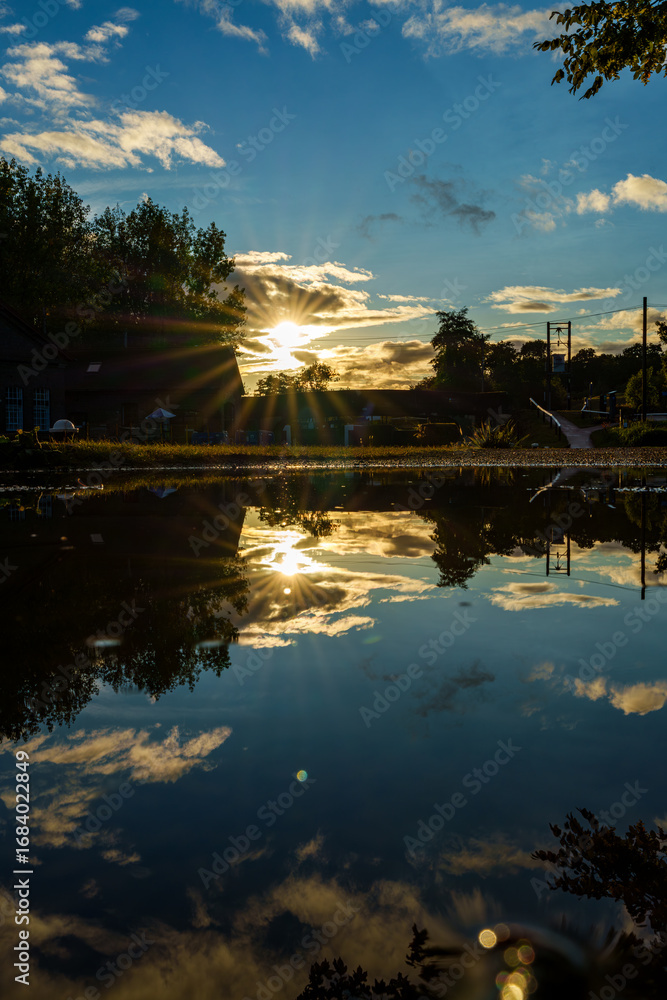 Fototapeta premium Sunset reflecting on water surface with clouds and trees
