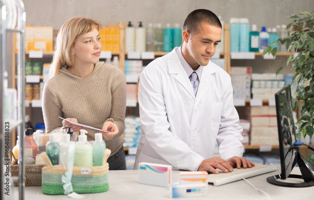 Obraz premium Man pharmacist is working at computer, collaborate with girl client.Electronic database of drugs, international classification of diseases. Detailed list of drugs for treatment of colds.