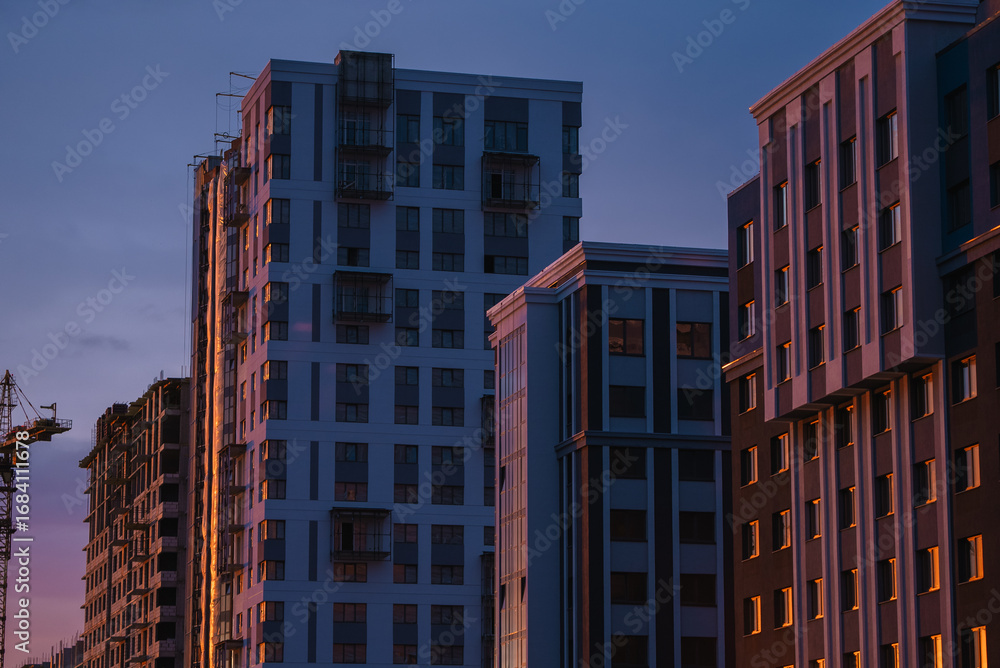 Fototapeta premium Newly constructed residential buildings stand tall against the backdrop of a vibrant sunset, their facades reflecting the warm hues of the evening sky, creating a captivating urban landscape