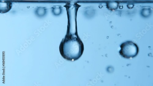 A close up shot of bubbles rising in clear blue liquid with light reflecting on their surfaces