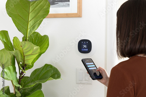 Woman programming a smart thermostat. Using a smartphone to program a thermostat