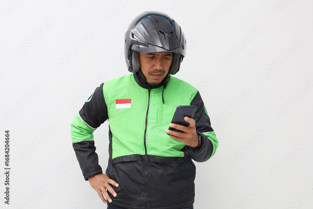 Fototapeta premium Asian online taxi driver wearing green jacket and helmet using mobile phone while thinking
