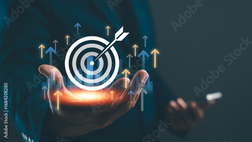 A hand holds a target symbol with arrows indicating growth, symbolizing goal achievement and success in business or personal development.