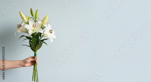 Hand holding a bouquet of white lilies against a light blue background