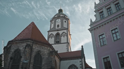 Frauenkirche tower in Meißen, Germany, with clock face and Gothic details, framed by colorful old town buildings under a clear sky.