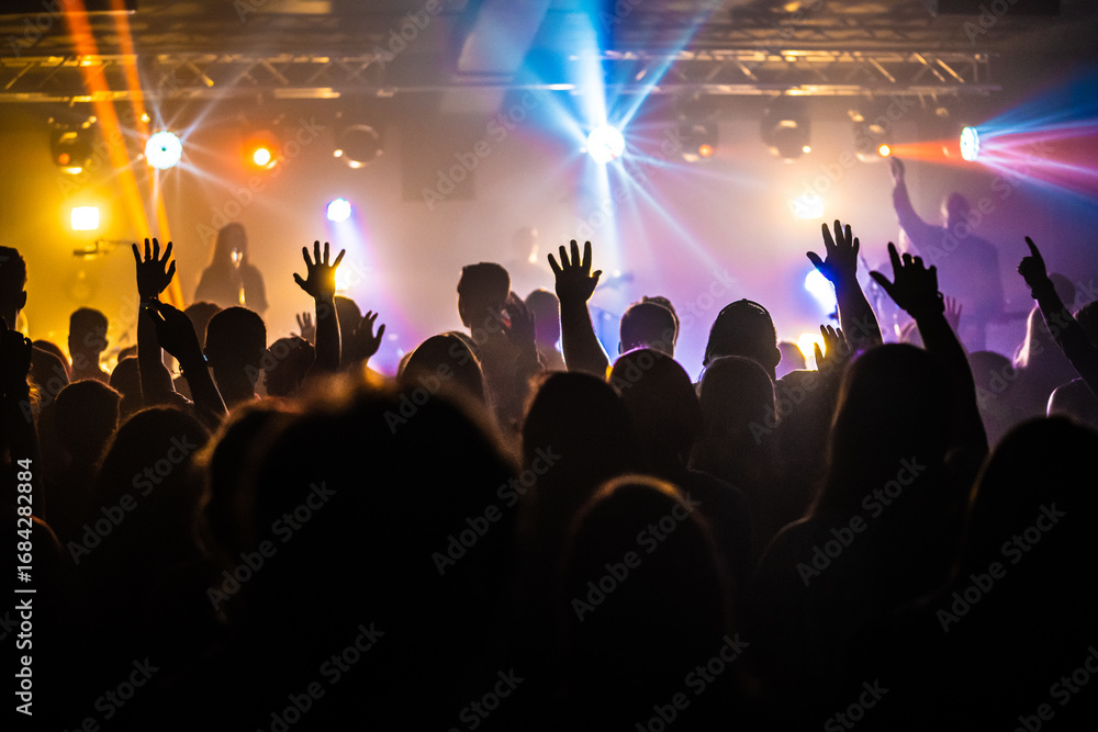 Fototapeta Group of Teenagers Worshiping with Arms Raised Under Concert Lighting