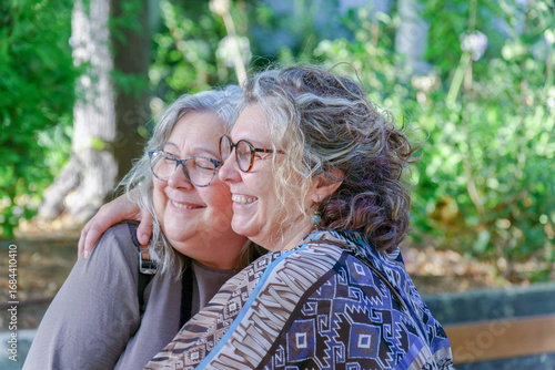 Two happy senior women hug in a park, enjoying a tender moment of affection and companionship, representing lgbtq love and visibility