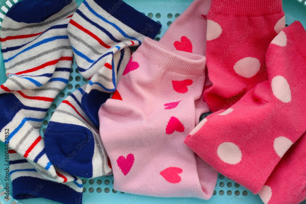 Fototapeta premium Mixed colorful socks with polka dot, stripe, and heart patterns in a laundry basket.