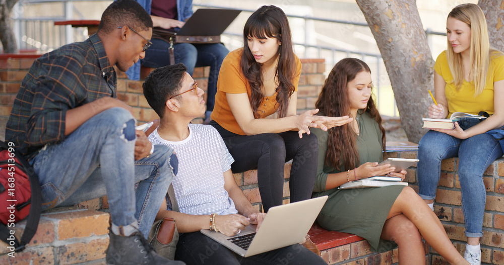 Obraz premium People, students and talk with laptop at campus for education, research and group project. Friends, pc and textbook for learning, university scholarship and studying information for exam preparation
