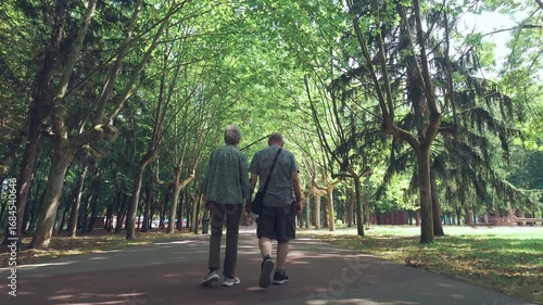 Wallpaper Mural An elderly couple walk through a beautiful city park lined with trees on a sunny day while holding hands. Full length body, rear, follow shot. Torontodigital.ca