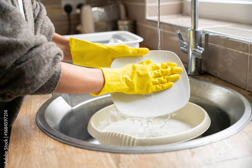 Quadro su tela Person does dishes in a home kitchen during daytime, wearing yellow gloves and f