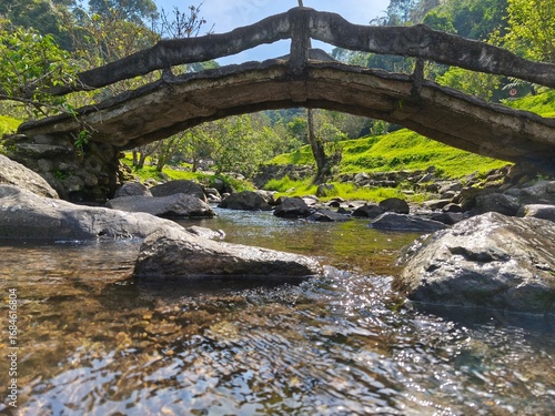 Stone bridge over a calm stream in a lush green valley.