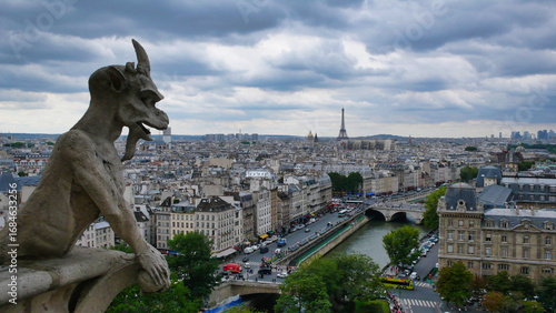 Gargoyles of Notre Dame overlooking Paris: The iconic gargoyles of Notre Dame Cathedral gaze out over the Parisian cityscape on a dramatic and cloudy day.