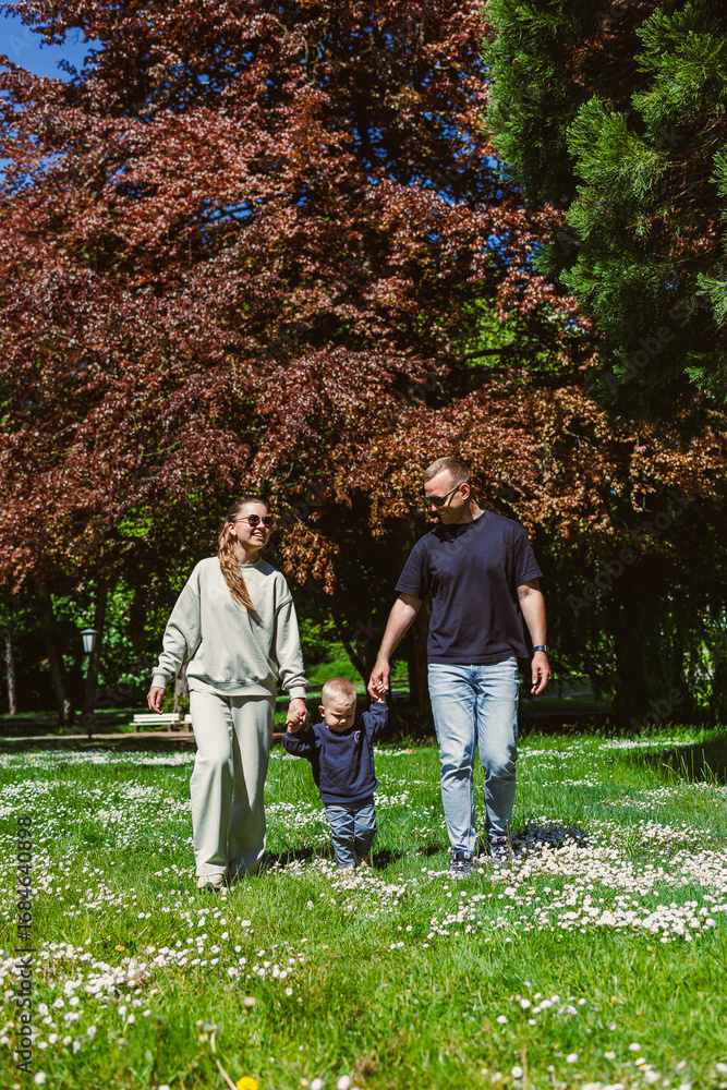 Fototapeta premium On a sunny day, a happy family of four enjoys time together in a vibrant park, sharing laughter, playing games, and making memories amidst the beautiful nature and blooming flowers