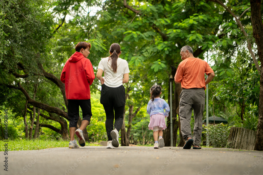 Fototapeta premium Asian family jogging together in the park. Parents, child, and grandfather exercising outdoors