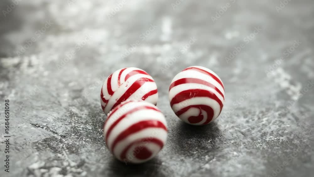 Three red and white striped round peppermint candies on grey surface