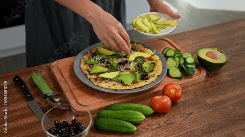 Woman adding avocado slices to vegetarian vegetable pizza. Healthy, delicious food close-up.