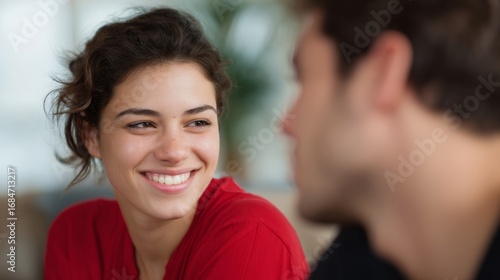 A woman smiles warmly at a man, creating a moment of connection. The background is soft and blurred, emphasizing their interaction. The image showcases joy and companionship. AI