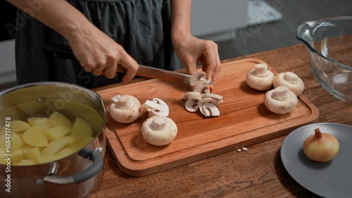 Woman cutting mushrooms on wooden board. Close-up, kitchen prep.