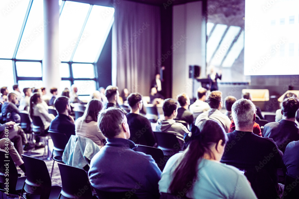 Obraz premium Speaker giving a talk in conference hall at business event. Rear view of unrecognizable people in audience at the conference hall. Business and entrepreneurship concept