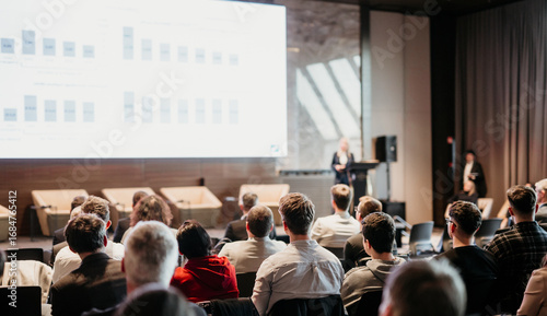 Female speaker giving a talk on corporate business conference. Unrecognizable people in audience at conference hall. Business and Entrepreneurship event