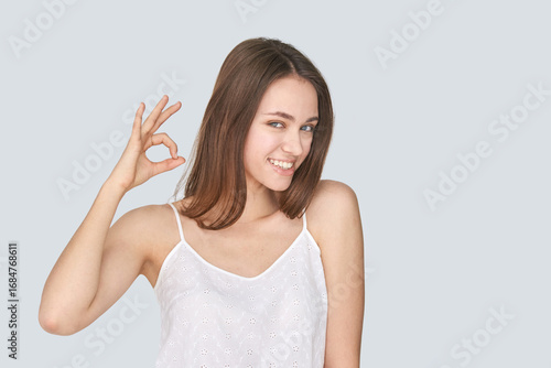 Wallpaper Mural Smiling young caucasian female making ok gesture in white top against light background. Torontodigital.ca