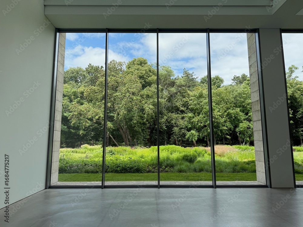 Obraz premium Beautiful green trees and other different plants under blue sky, view through panoramic windows