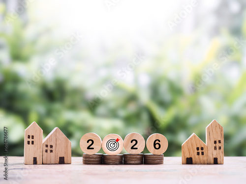 Miniature house and wooden blocks with number 2026 on stack of coins. The concept of saving money for house, Property investment, House mortgage, Real estate in year 2026.