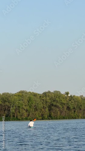 A person navigates gently on a calm lake, surrounded by vibrant trees and nature, enjoying a peaceful day of kayaking under a clear blue sky.