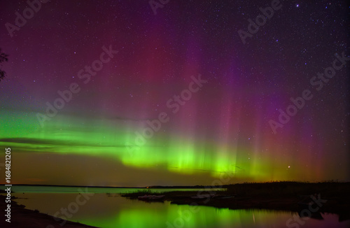 Wallpaper Mural Vivid green and purple aurora lights shimmer across the starry night sky, reflecting on calm lake waters with a peaceful horizon view. Torontodigital.ca