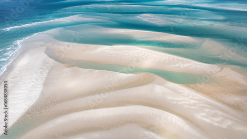 Aerial view of shifting sands create a mesmerizing dance of light and shadow where turquoise waters meet the bleached shore, Moreton Island, Queensland, Australia.