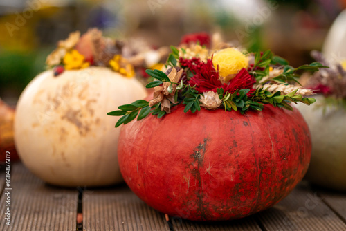 View of ripe pumpkins decorated with colorful flowers. Halloween decor. Holiday decor with pumpkins and flowers