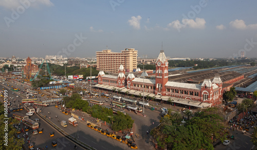 Aerial view of the vibrant red and white brick Chennai Central Railway Station contrasting against the bustling city streets and lush greenery, Chennai, Tamil Nadu, India.