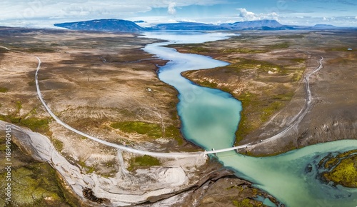 Aerial view of a glacial river winding through rugged terrain, its turquoise waters contrasting against the barren landscape, Hvita, BlÃ¡skÃ³gabyggÃ°, Iceland.