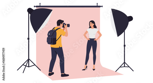 A photographer with a backpack takes a picture of a female model in a studio setting with two studio lights and a pink backdrop.