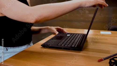 Faceless woman opening a laptop computer at wooden desk for work in office space. Concept of remote work, business productivity, online tasks, modern communication and efficiency.