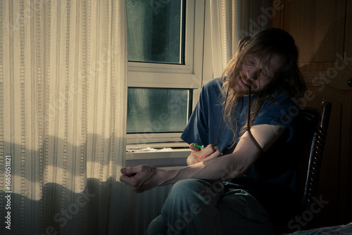 The High and The Low. A drug user injecting himself in a darkened room. The image evokes feelings of addiction, drug abuse, and dependence.