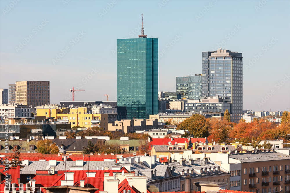 Obraz premium Warsaw skyline featuring modern glass skyscrapers alongside colorful rooftops of historic buildings. Vibrant cityscape captures the dynamic blend of tradition and progress in Poland capital