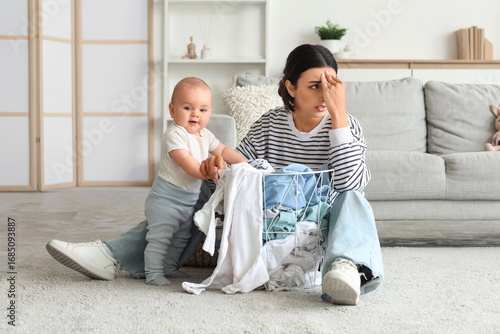 Young mother suffering from postnatal depression with dirty laundry and her b...
