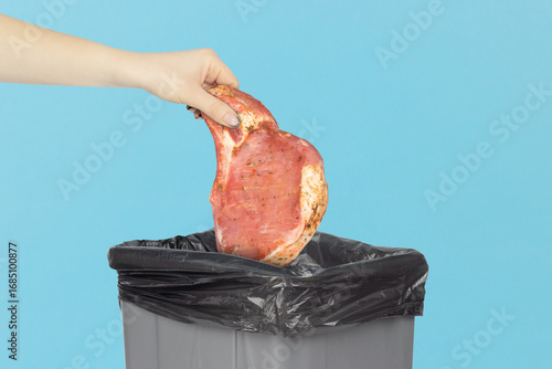 throwing raw marinated steak into the trash, reaching hand with raw marinated steak to trash can, vegetarianism concept