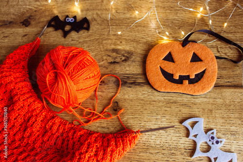 Orange wool and knitting needles with decorative pumpkin and bat. Halloween still life. Cozy lifestyle concept. Autumn lifestyle. October background. Bright needlework and smiling pumpkin. 
