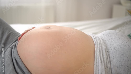 Close-up of a pregnant woman belly with visible baby movements. Expecting mother lying on her back, gently stroking her stomach. Intimate and emotional moment of pregnancy,