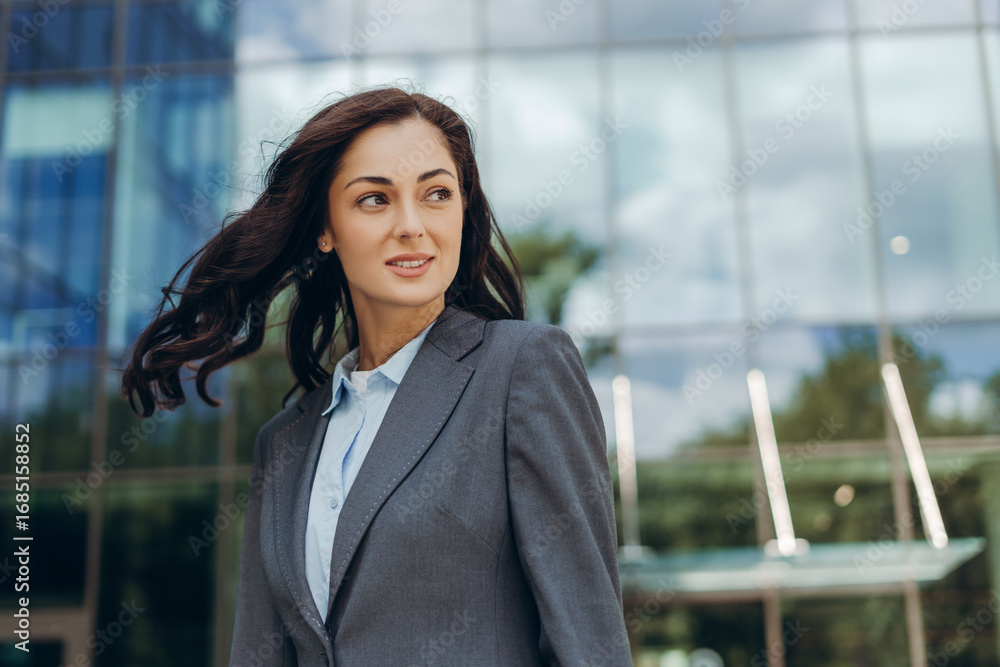 Fototapeta premium Businesswoman smiling and looking away with hair blowing in wind in front of office building