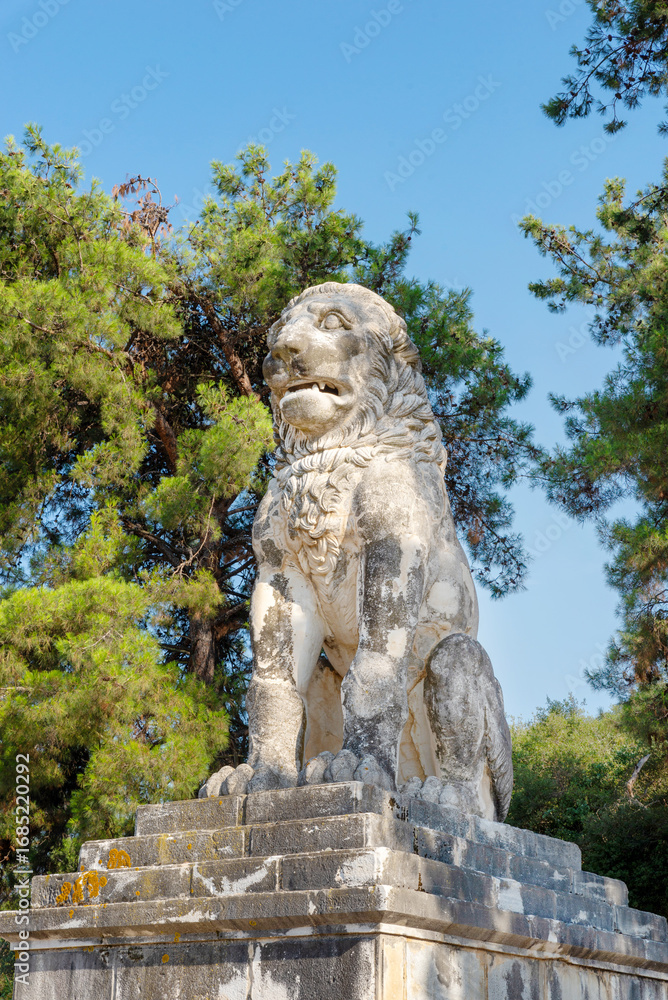 Obraz premium Ancient Lion of Amphipolis statue in Greece under clear blue sky surrounded by pine trees