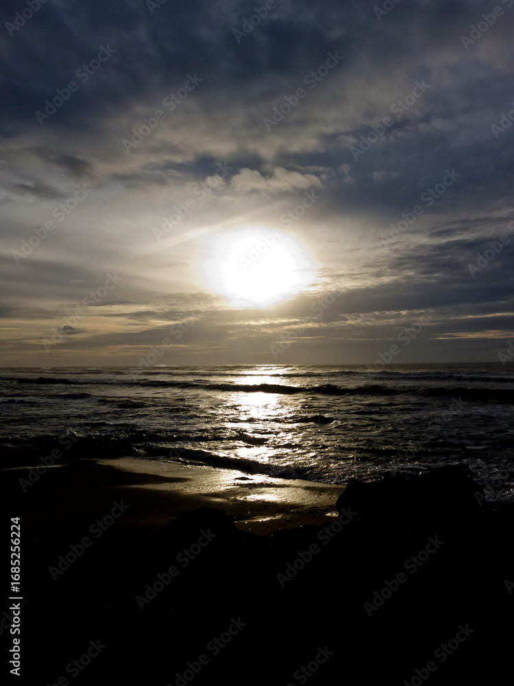 Obraz premium A bright sun shining over the ocean with dark clouds in the sky.